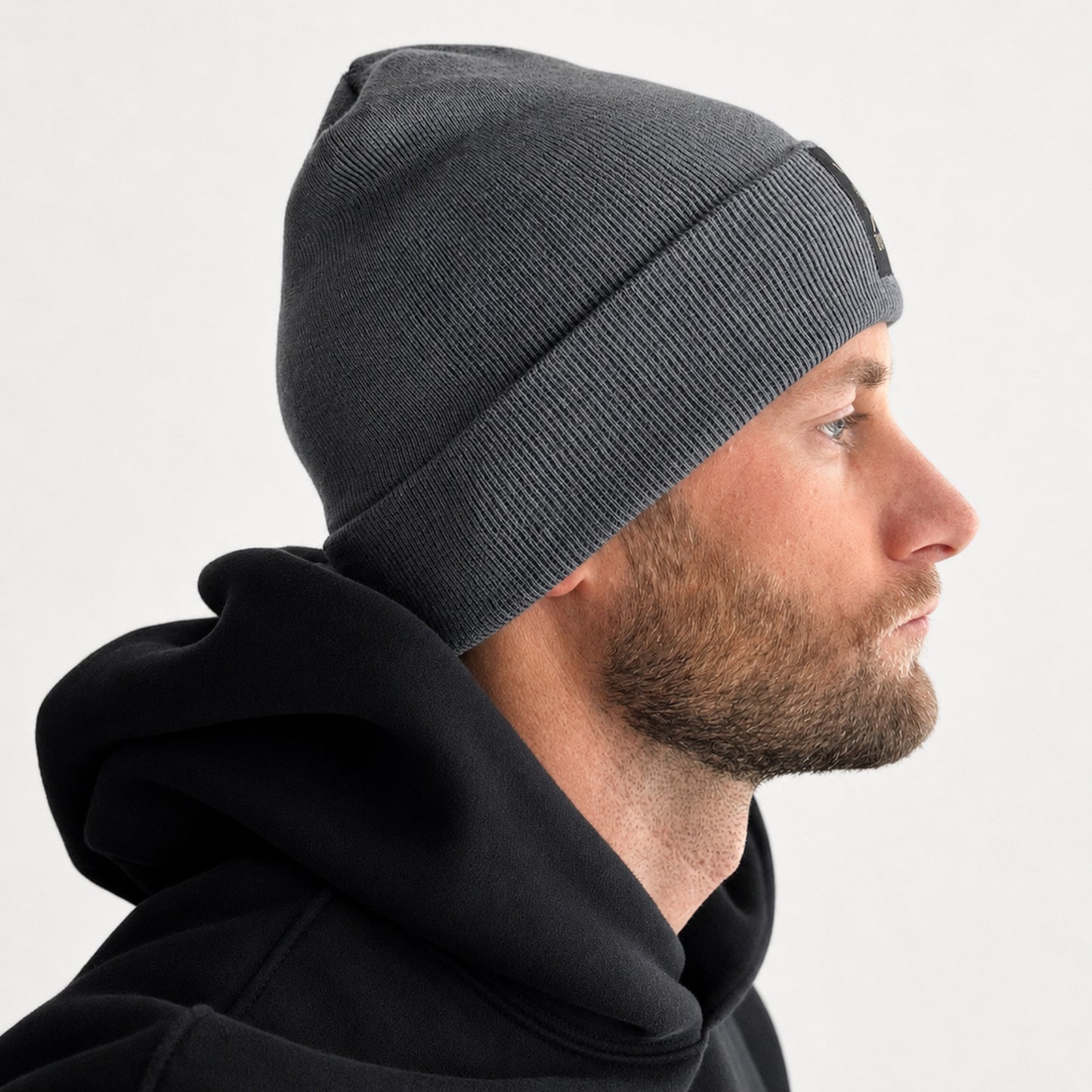 Mann trägt graue Gym Beanie im Profil – Gym Generation Wintermütze mit umgeschlagenem Bund zu schwarzem Hoodie im Streetwear-Look