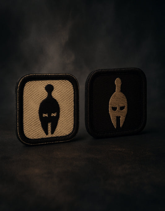 Spartaner Patch Zweier-Set mit Klettverschluss in Sand- und Schwarz-Design, Premium Stickqualität, fotografiert vor dunklem taktischem Hintergrund, ideal für Tactical Gear, Gym-Bags und Outdoor-Equipment.