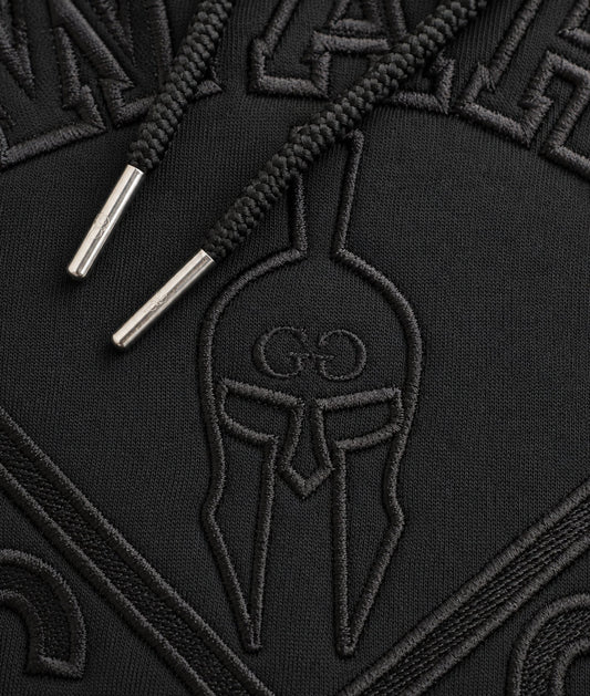 Detailaufnahme der schwarzen Gym-Warriors-Stickerei und des Kordelzugs mit silbernen Metallkappen