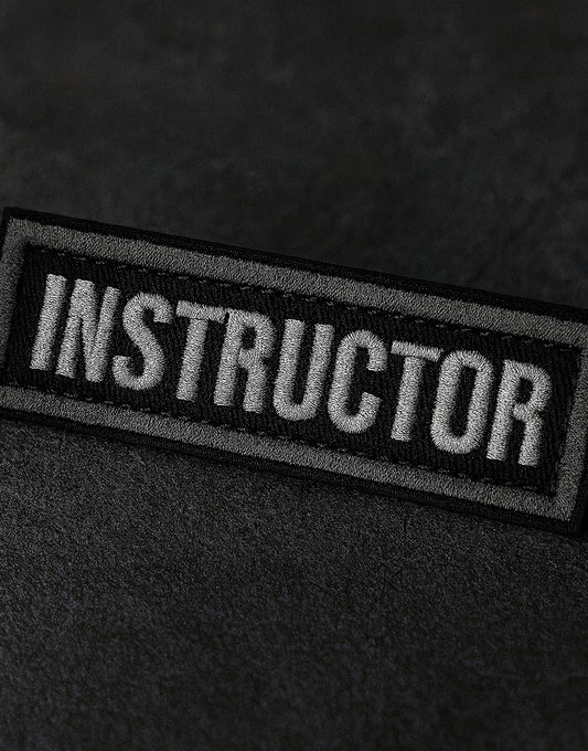 Instructor Patch in Schwarz-Grau mit weisser Bestickung und Klettverschluss, ideal für Trainer, Coaches und Ausbilder im taktischen Einsatz, militärischen Bereich oder Fitness, robustes Tactical Patch für Westen, Rucksäcke und Uniformen von Gym Generation.