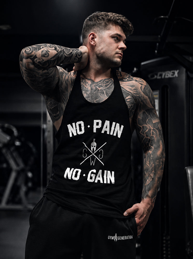 Tätowierter Athlet im schwarzen Gym Generation Stringer No Pain No Gain in einem dunklen Gym – weisser Frontprint mit Schriftzug No Pain No Gain, Spartaner-Helm und gekreuzten Linien, ärmelloses Bodybuilding-Shirt für Herren mit tiefem Racerback-Rücken