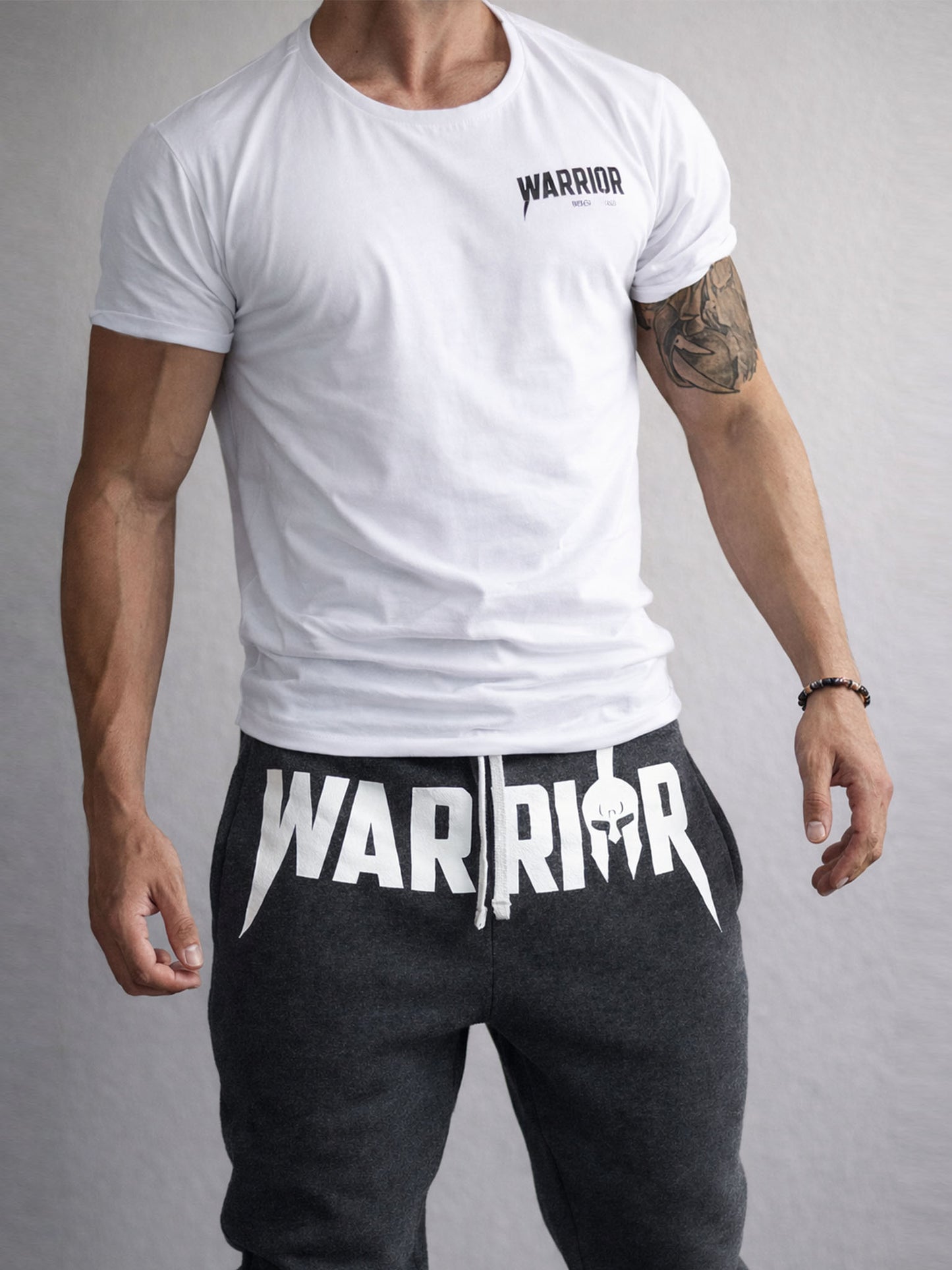 Detailansicht der dunkelgrauen Warrior Jogginghose für Herren mit großem weißen Warrior Print und passendem weißen Gym T-Shirt