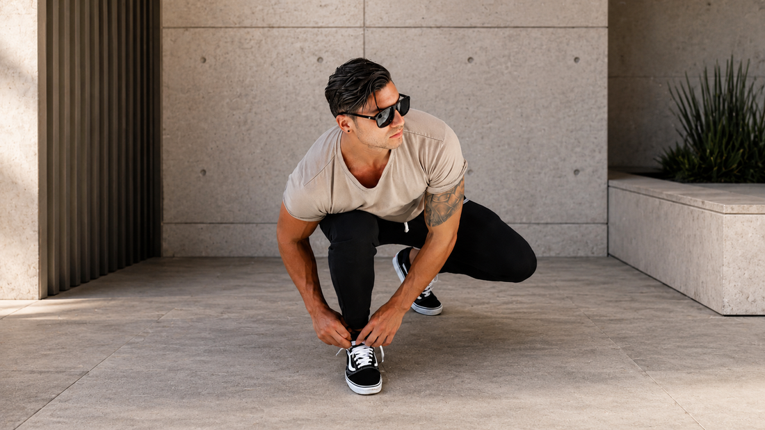 Athlet trägt ein Gym Generation Herren Fitness Outfit mit beigem T-Shirt und schwarzer Hose in urbaner Lifestyle-Umgebung.