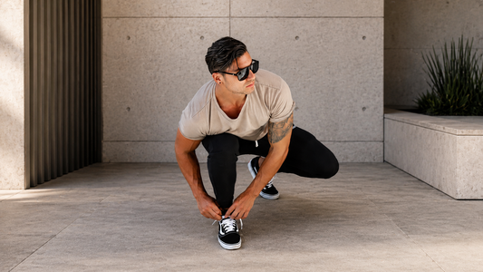 Athlet trägt ein Gym Generation Herren Fitness Outfit mit beigem T-Shirt und schwarzer Hose in urbaner Lifestyle-Umgebung.