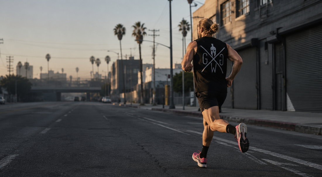 Athlet läuft bei Sonnenaufgang durch eine leere Strasse in Los Angeles und trägt einen schwarzen Gym Generation Stringer mit Rückenlogo.