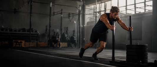 Athlet beim Sled Push in einem dunklen Functional-Fitness-Gym als Symbol für Hybrid Training, Kraftausdauer und Wettkampfvorbereitung.