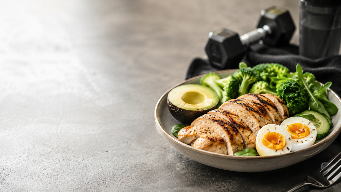 Low Carb Muskelaufbau Mahlzeit mit Poulet, Eiern, Avocado und Gemüse neben Hantel und Shaker