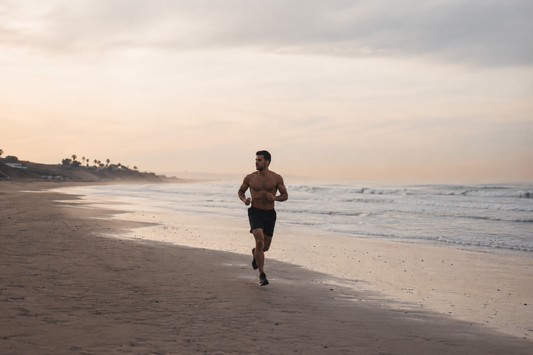 Athletischer Mann läuft oberkörperfrei am Strand als Symbol für Cardio, Ausdauertraining und Fitness-Lifestyle
