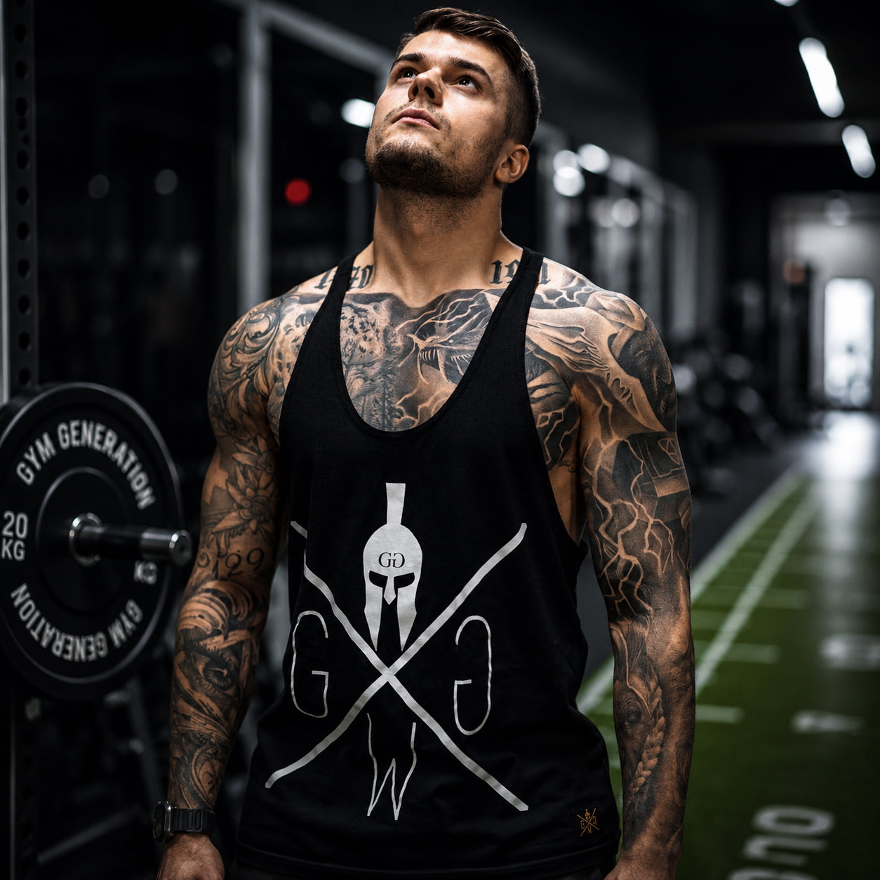 Athlet trägt schwarzes Stringer Tank Top mit Gym Warriors Logo im Gym – Gym Generation