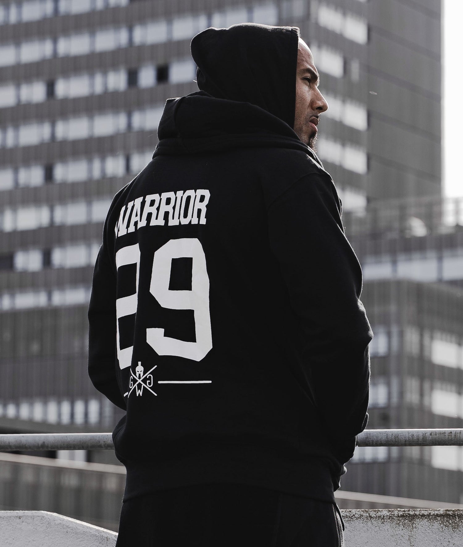 Warrior Trainingsbekleidung für Athleten und Kampfsportler – Mann trägt schwarzen Warrior Hoodie, Rückenansicht, urbaner Outdoor-Look.