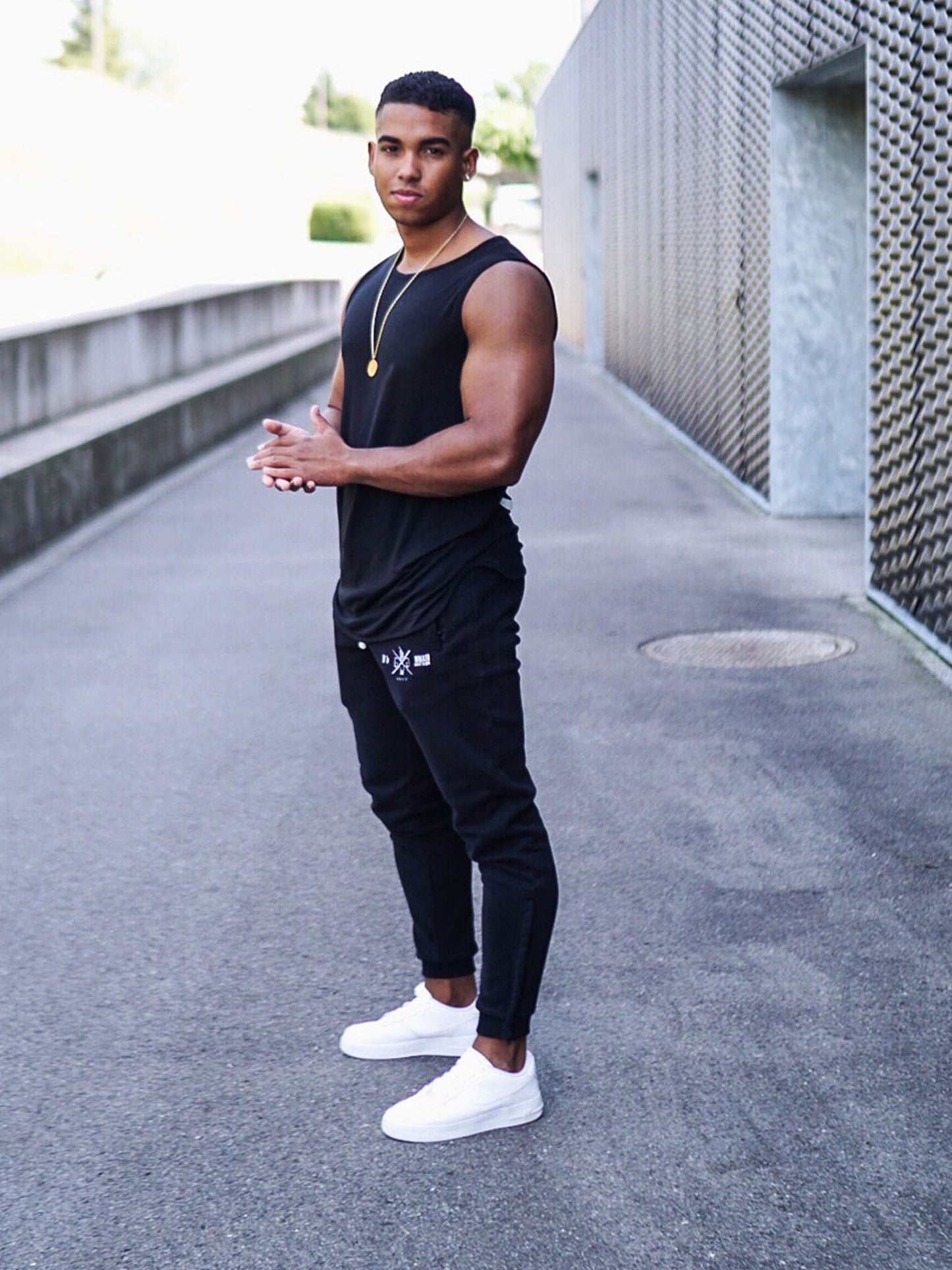 Athlet in schwarzem Gym Generation Fitness Tank Top 'Warrior' und Jogginghose, posiert im modernen Outdoor-Setting.