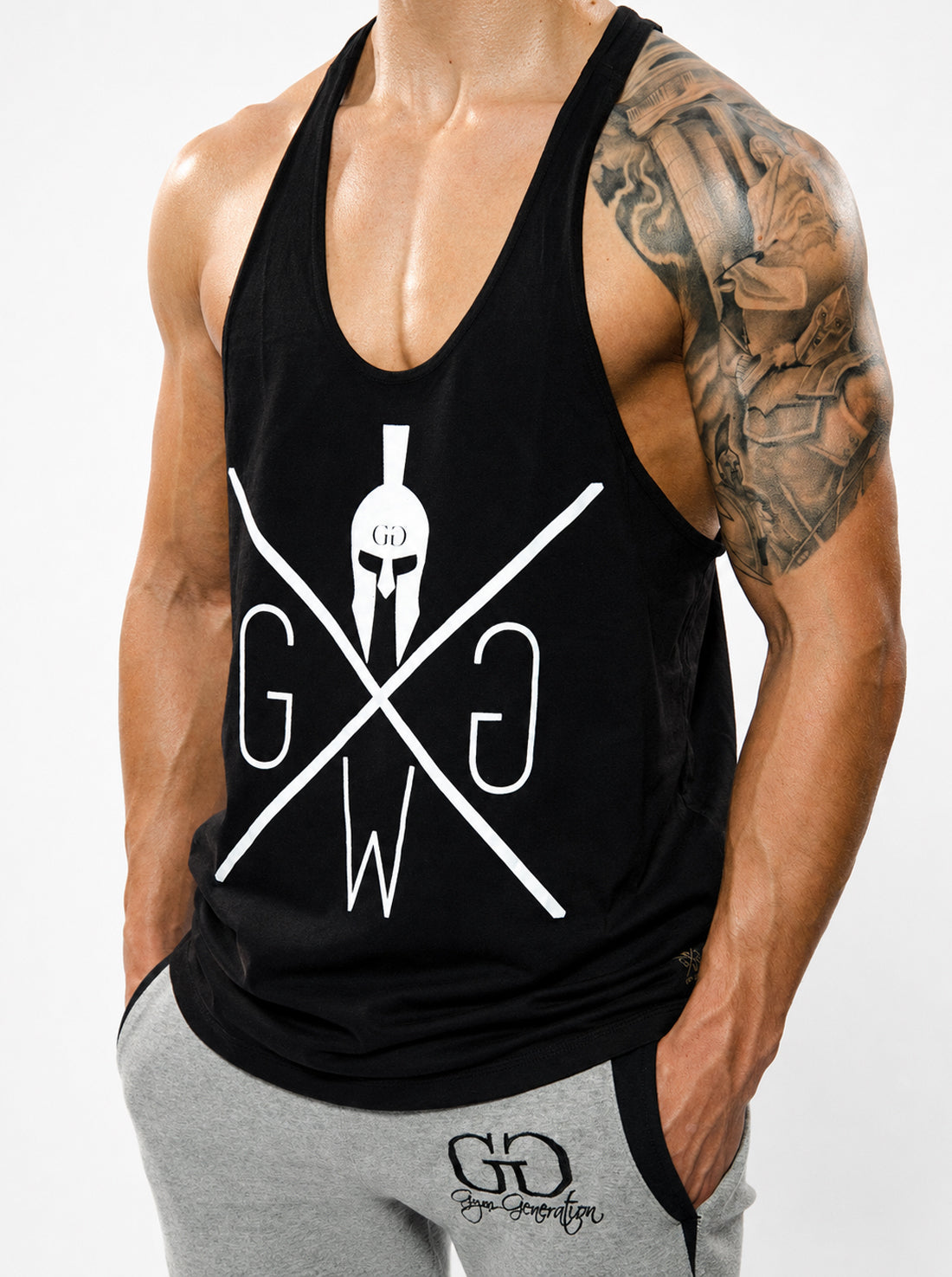 Gym Generation Stringer schwarz mit weissem Spartan-Print, getragen von einem muskulösen Athleten im Studio