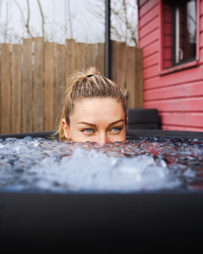 Frau taucht ihren Kopf in eine Eistonne mit Eiswasser ein, ideal für Kältetherapie, Regeneration und mentale Erfrischung zu Hause.