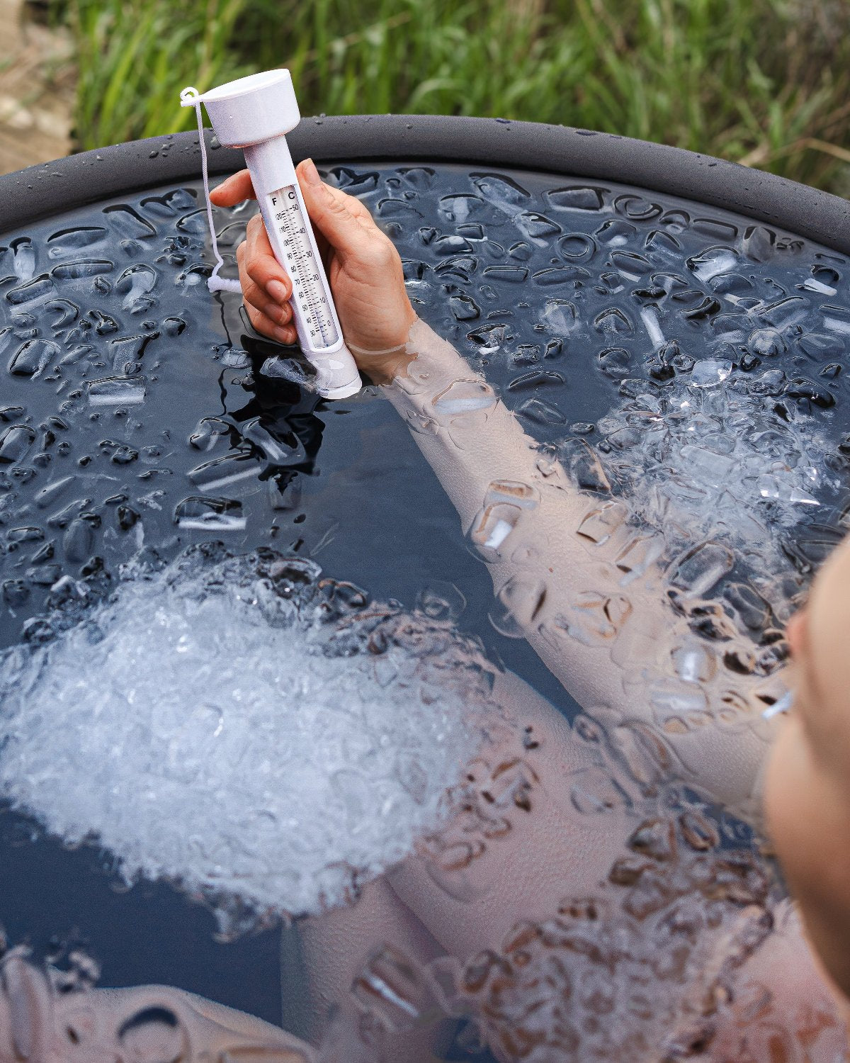 Nahaufnahme einer Hand, die ein Thermometer in eisigem Wasser eines Eisbades hält, ideal für Kältetherapie und präzise Temperaturkontrolle zu Hause.