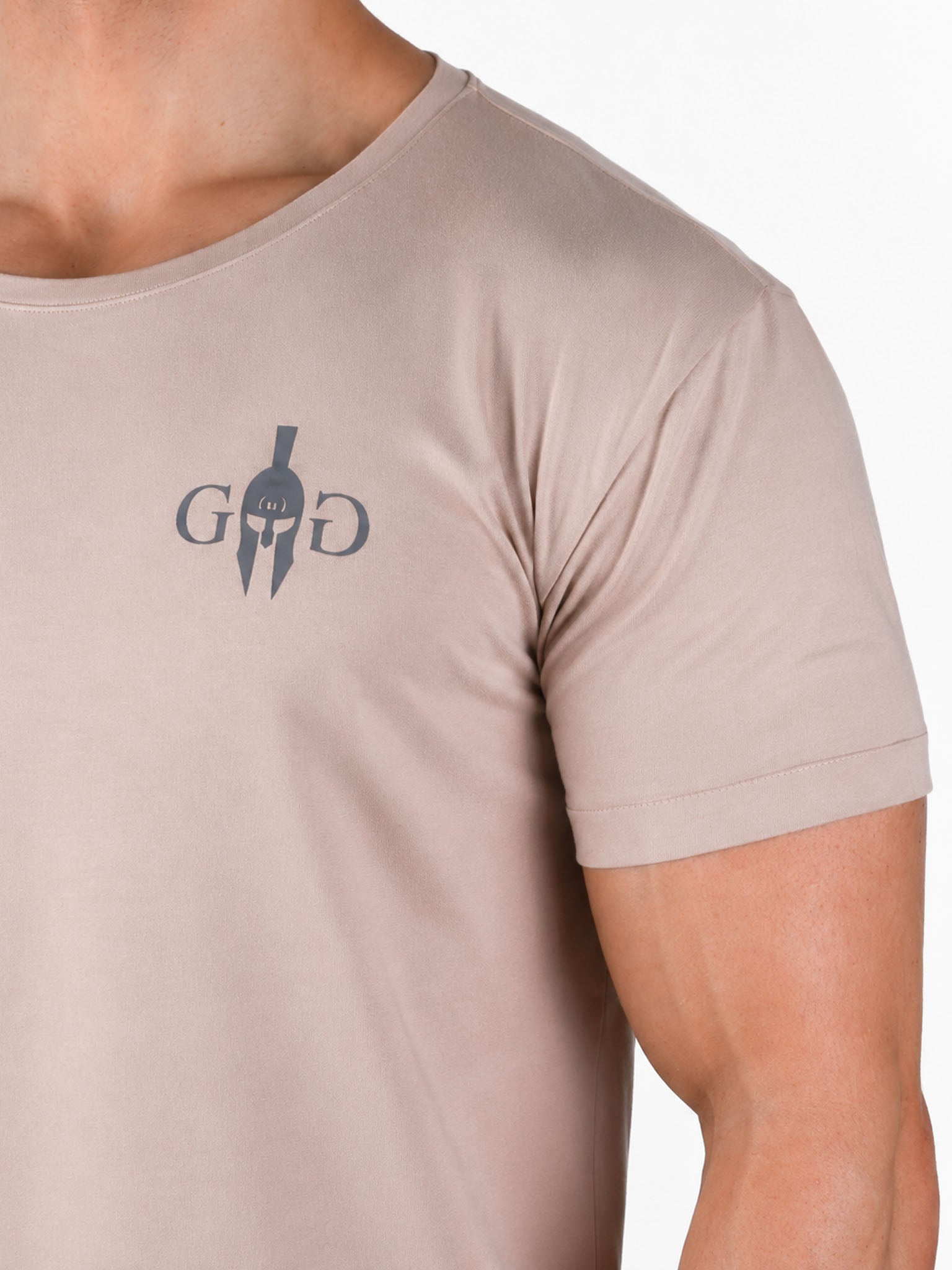 Detailansicht des Spartaner-Emblems mit GG-Initialen auf dem beigen Fitness T-Shirt 'Club' von Gym Generation – dunkler Print auf leichter Baumwollmischung in Nahaufnahme