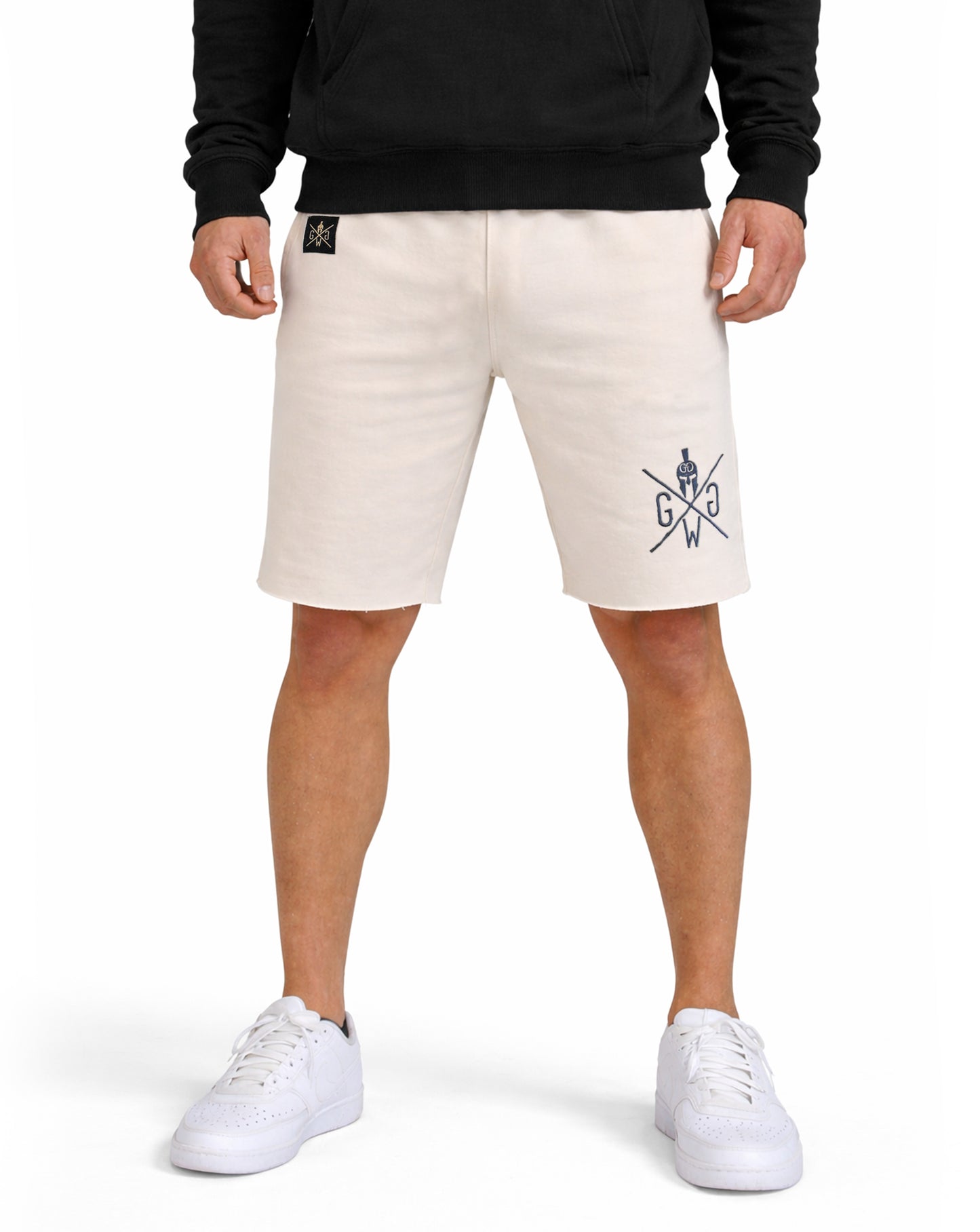 Beige Gym Shorts Herren von Gym Generation in Frontansicht im Outfit – sportliche Fitness Shorts am Model kombiniert mit schwarzem Hoodie und weißen Sneakers