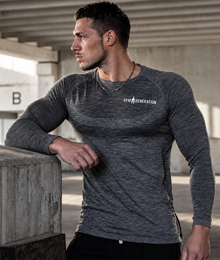 Langarm Sportshirt Herren Dunkelgrau am Model, seitlich an Betonmauer gelehnt, mit Raglanärmeln und Schriftzug in Weiss