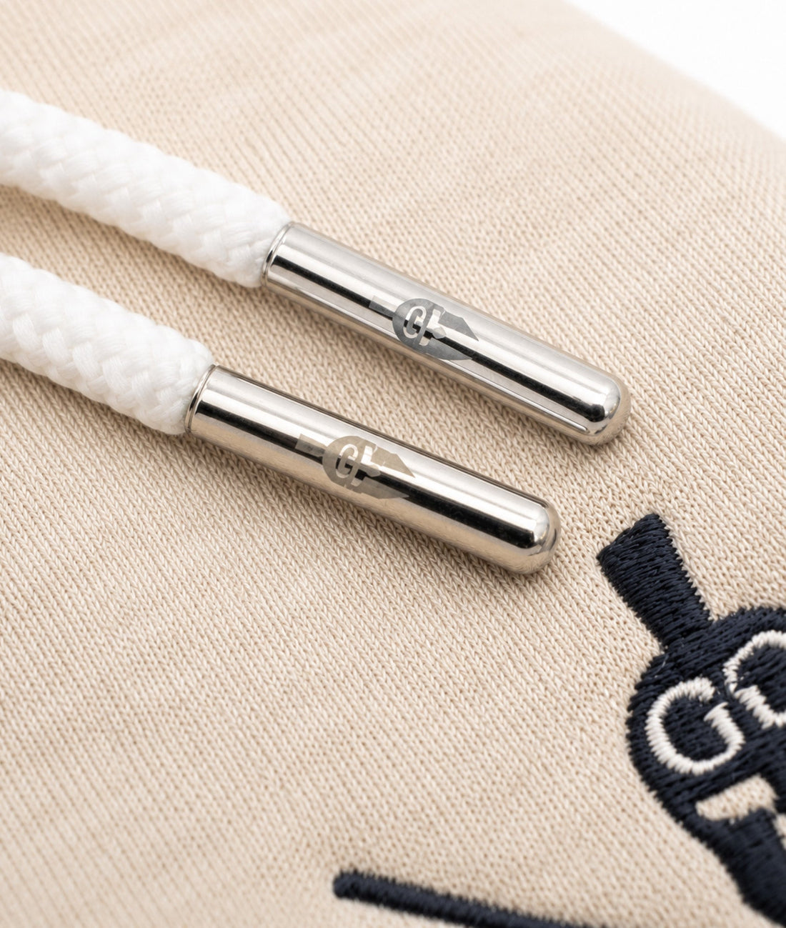 Weisse Hoodie-Kordeln mit gravierten silbernen Metall-Caps auf off-white Stoff, Premium Detailaufnahme von Gym Generation
