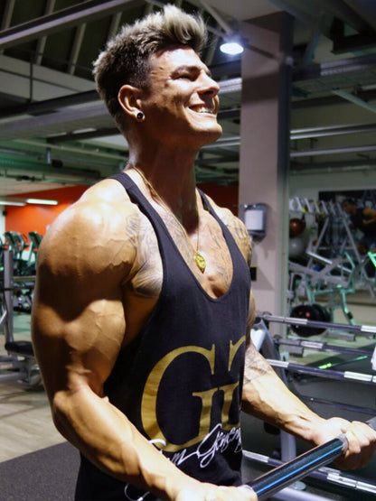 Bodybuilder beim Bizeps-Training mit Gym Generation Stringer Tank Top in Schwarz und goldenem Logo im Fitnessstudio.