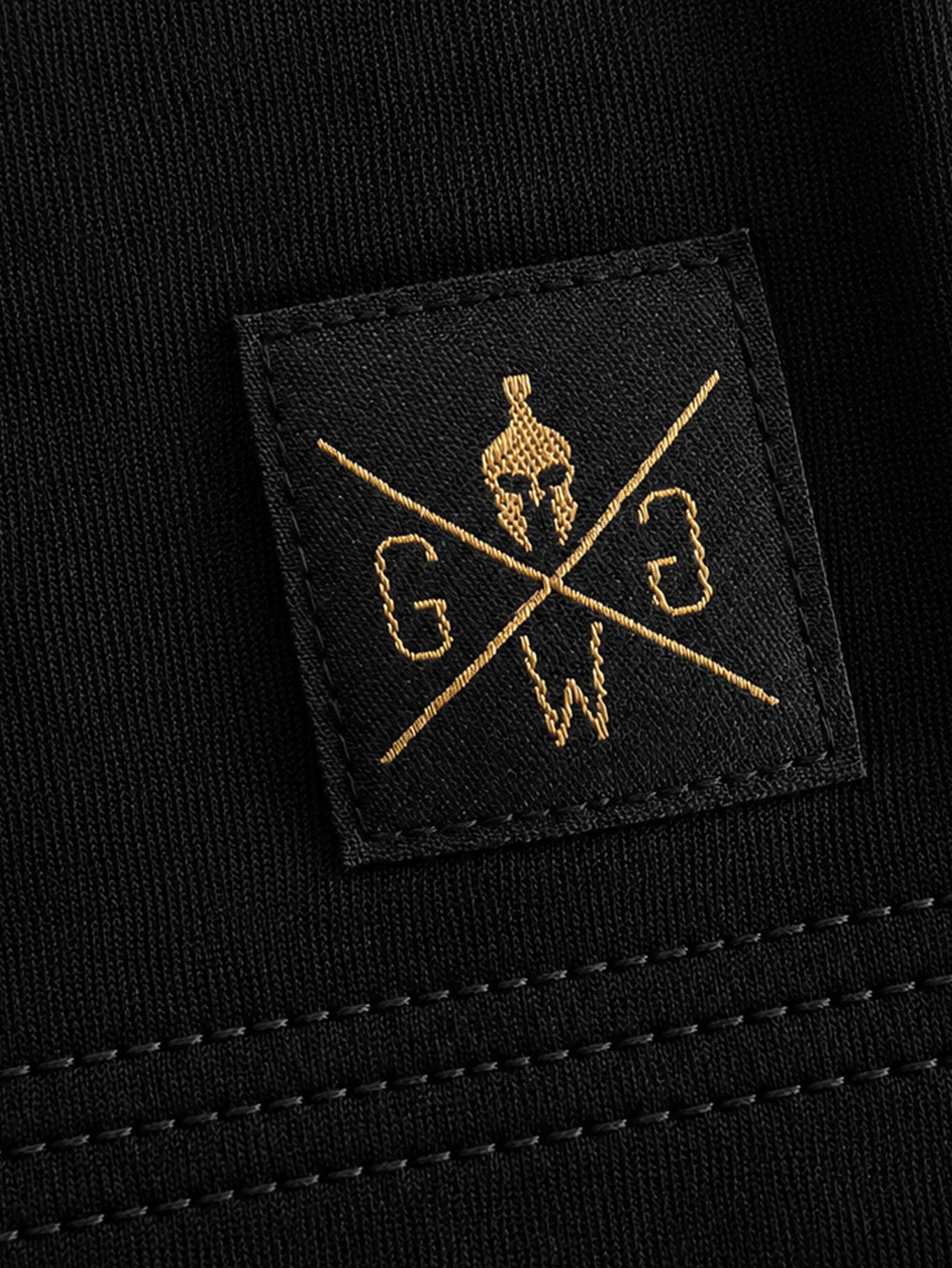 Gesticktes Gym Warriors Label am Saum des Gym Generation Stringer in Gold auf Schwarz
