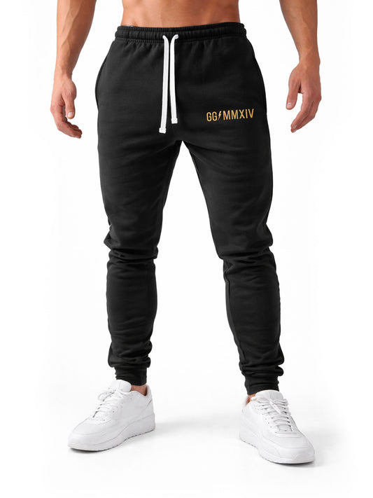 Frontale Studioaufnahme der Gym Generation Herren Trainerhose in Schwarz mit goldener GG MMXIV Stickerei und weißem Kordelzug, sportliche Trainingshose für Fitness und Krafttraining