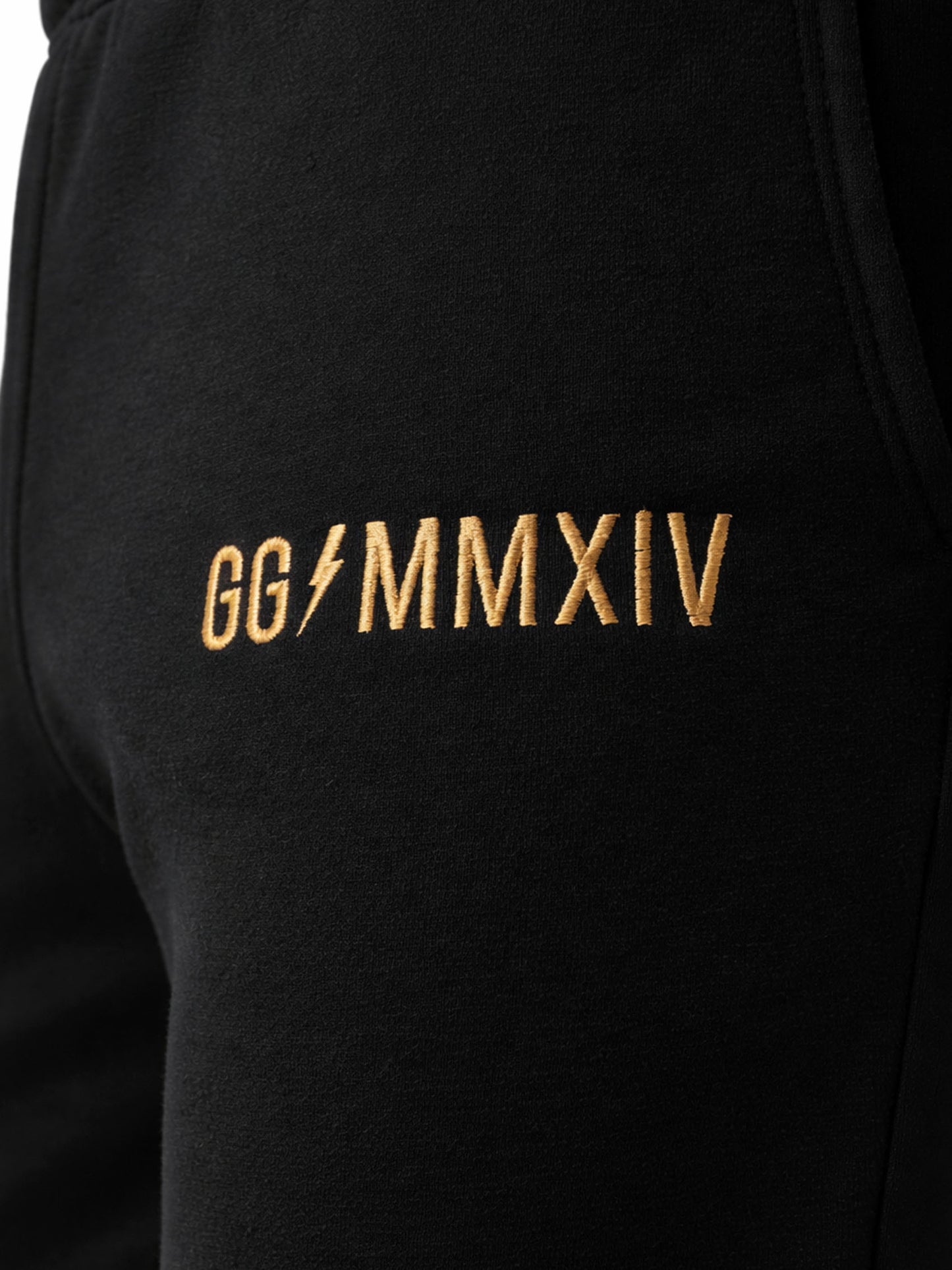 Detailaufnahme der Gym Generation Herren Trainerhose in Schwarz mit goldener GG MMXIV Stickerei, hochwertige Logo-Veredelung auf dem Stoff