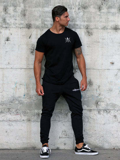 Schwarzes Fitness Outfit für Herren von Gym Generation – bestehend aus schwarzen Gym Sporthosen, schwarzem Gym T-Shirt und schwarzen Vans Schuhen. Ideal für Training und Freizeit, getragen von einem Fitness Model.