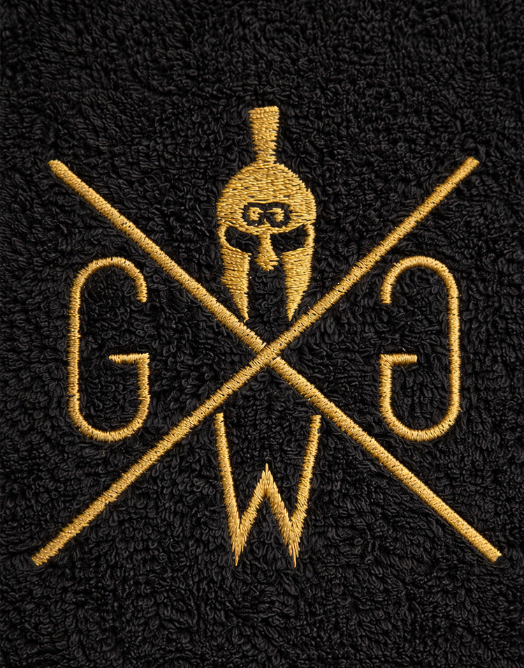 Detailaufnahme der goldenen Gym-Generation-Logo-Stickerei auf schwarzem Fitness-Handtuch.