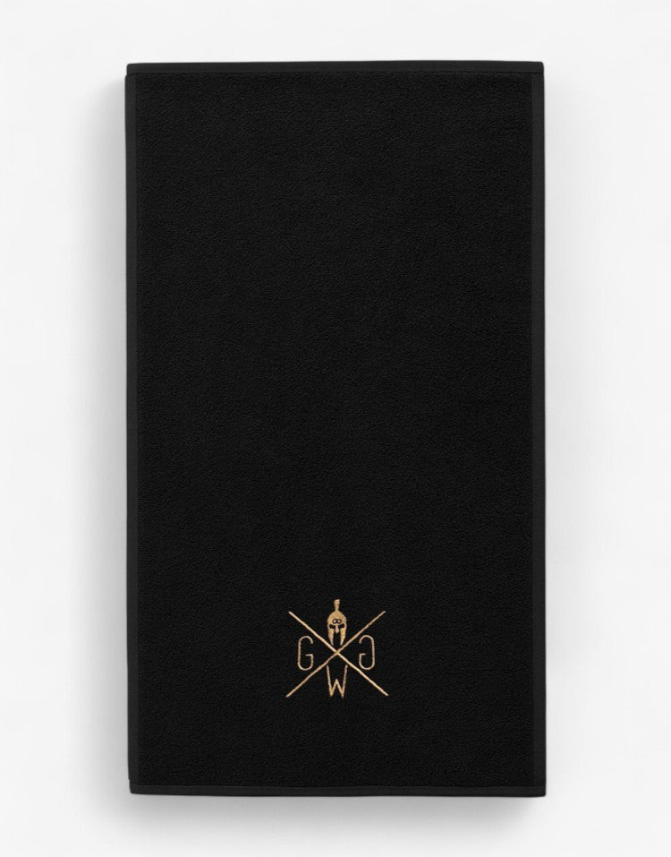 Baumwoll-Handtuch für Fitnessstudio, schwarz mit gold Logo, professionelle Produktaufnahme auf weißem Hintergrund – langlebiges Gym Handtuch.