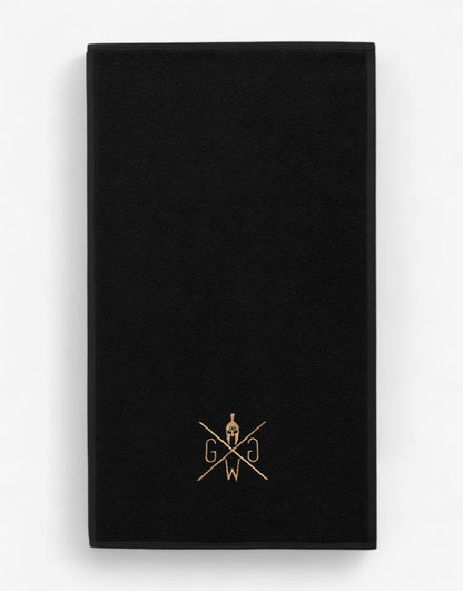 Baumwoll-Handtuch für Fitnessstudio, schwarz mit gold Logo, professionelle Produktaufnahme auf weißem Hintergrund – langlebiges Gym Handtuch.
