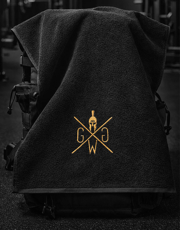 Schwarzes Gym Generation Fitness Handtuch im Gym Studio mit goldgesticktem Logo – hochwertiges Sporthandtuch für intensives Krafttraining