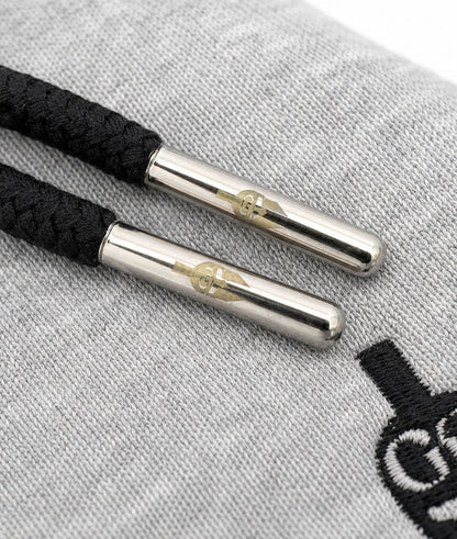 Silberne Kordel-Caps mit Gym Generation Gravur an schwarzen Hoodie Kordeln auf grauem Stoff, detailreiches Premium Close-up Produktbild auf weissem Hintergrund