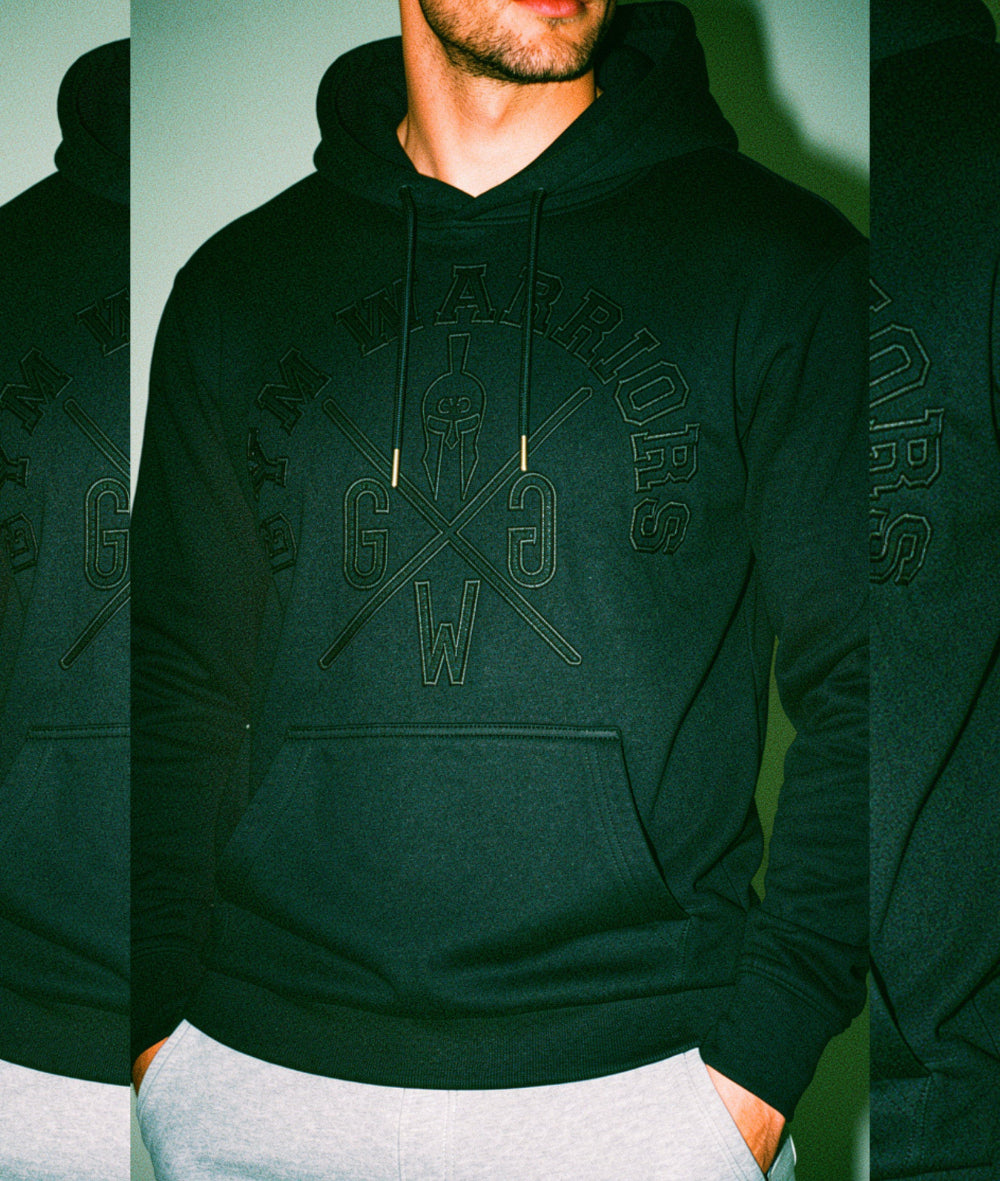 Mann trägt Gym Warriors Hoodie Herren in Schwarz mit ton-in-ton Stickerei und Kordelzug mit Silberkappen