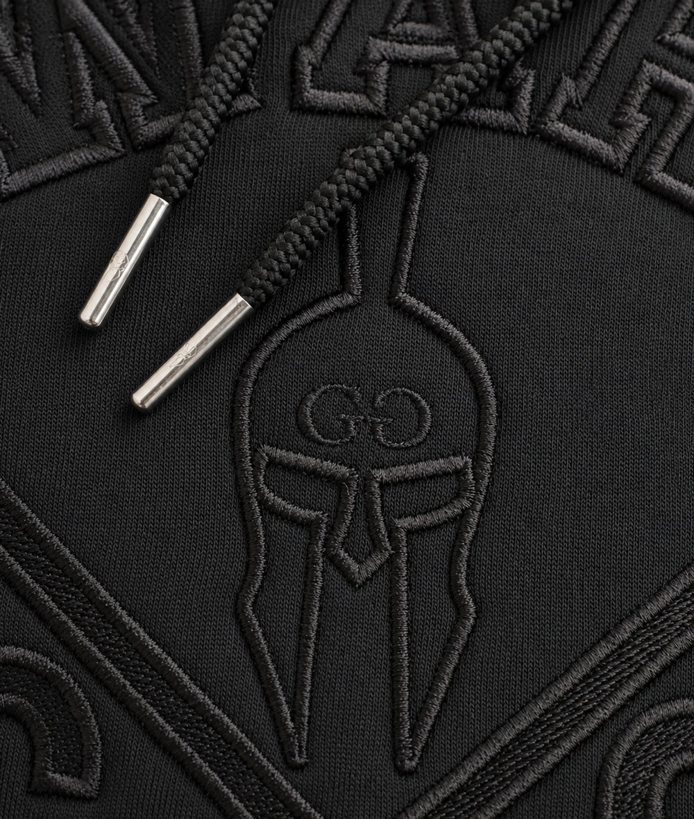 Detailaufnahme der schwarzen Gym-Warriors-Stickerei und des Kordelzugs mit silbernen Metallkappen