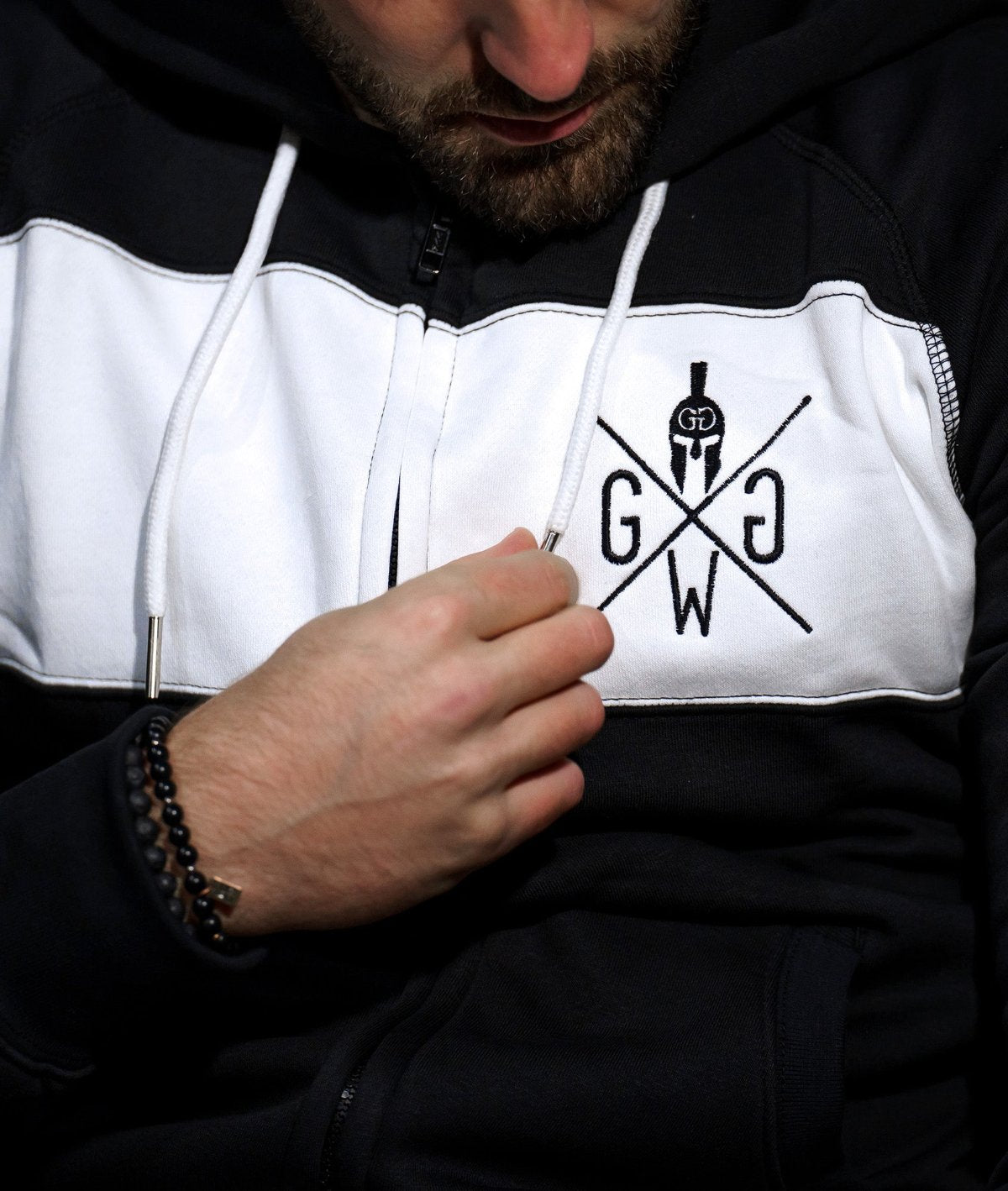 Nahaufnahme der Gym Generation Hoodie-Jacke mit weißem und schwarzem Design und Logo auf der Brust, Fokus auf den Reißverschluss und das detaillierte Branding.