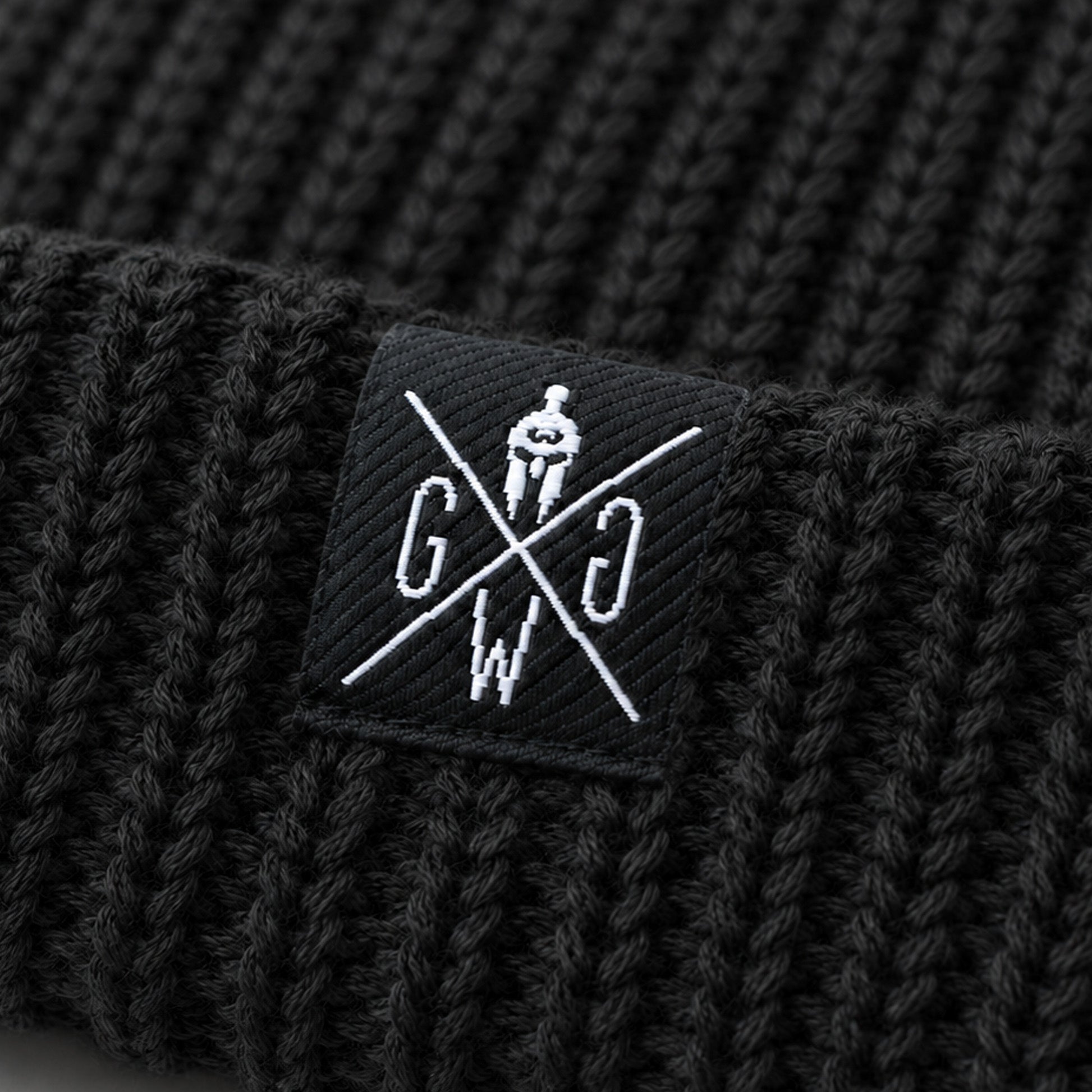 Gym Generation Logo-Patch auf schwarzer Beanie – Nahaufnahme der weissen Stickerei mit Spartaner-Helm auf grobem Rippstrick der Atlantic Mütze