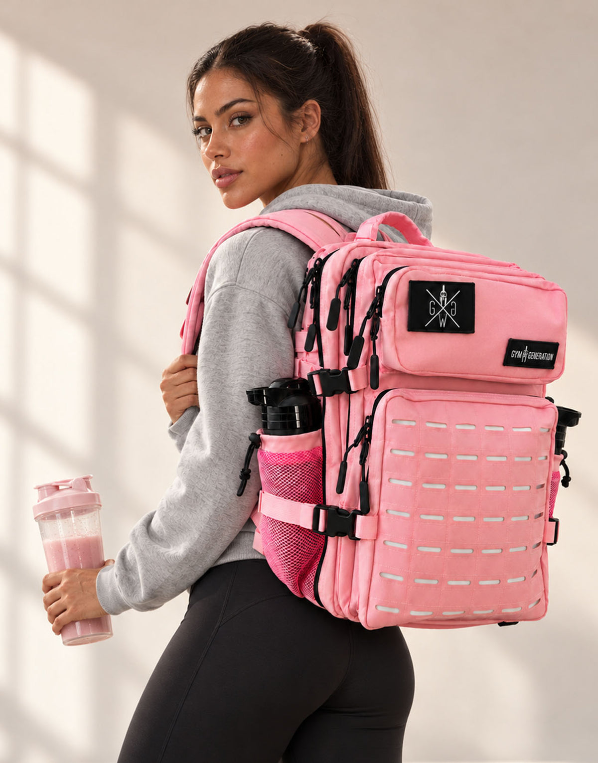 Frau trägt den Gym Rucksack Explorer in Cotton Candy Pink auf dem Rücken, Blick über die Schulter, mit pinkem Proteinshake in der Hand