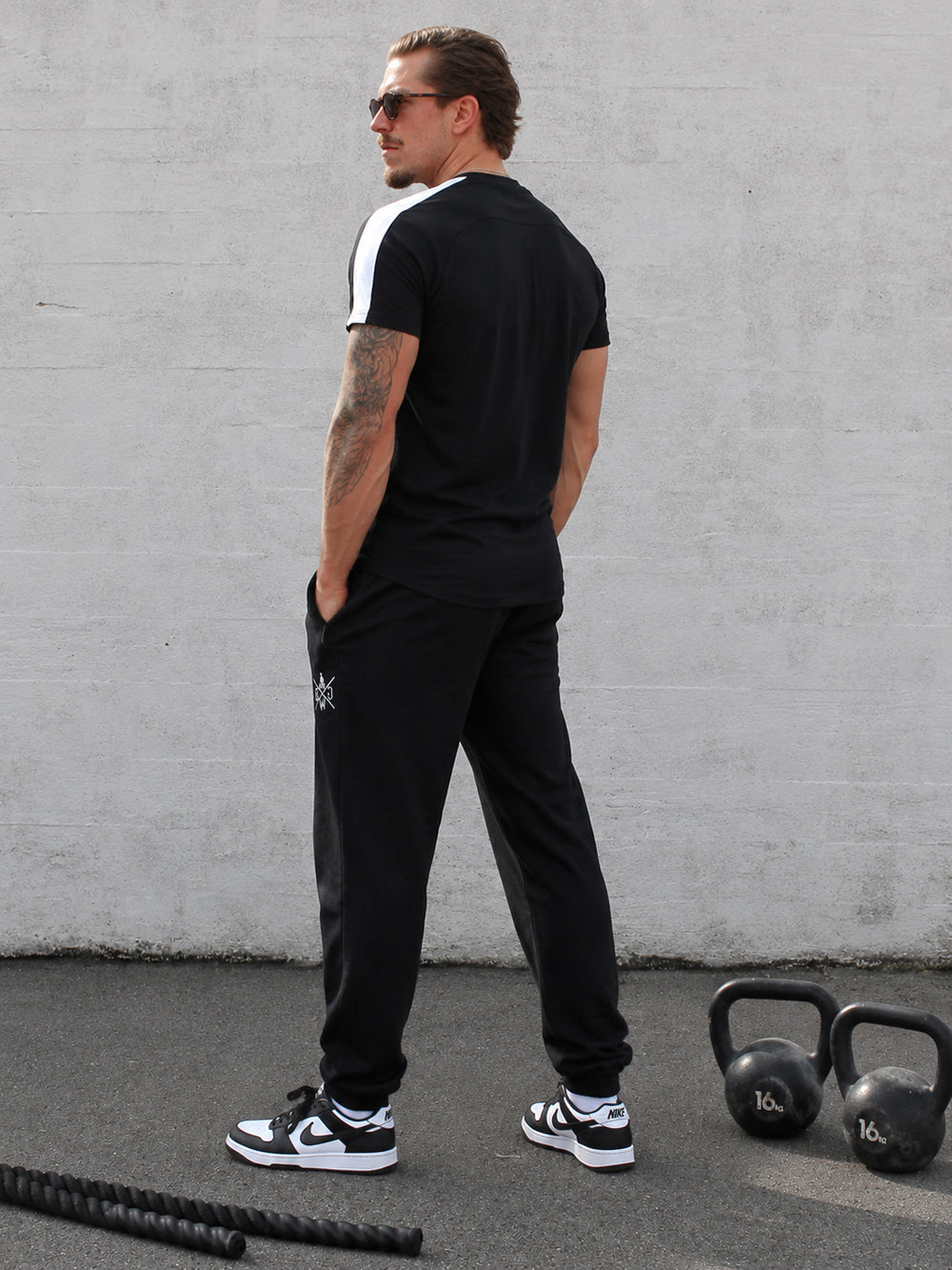 Schwarzes Gym Shirt Herren von Gym Generation in Rückenansicht am Model, sportlicher Streetstyle Look mit weissem Schulterstreifen und schwarzer Trainingshose