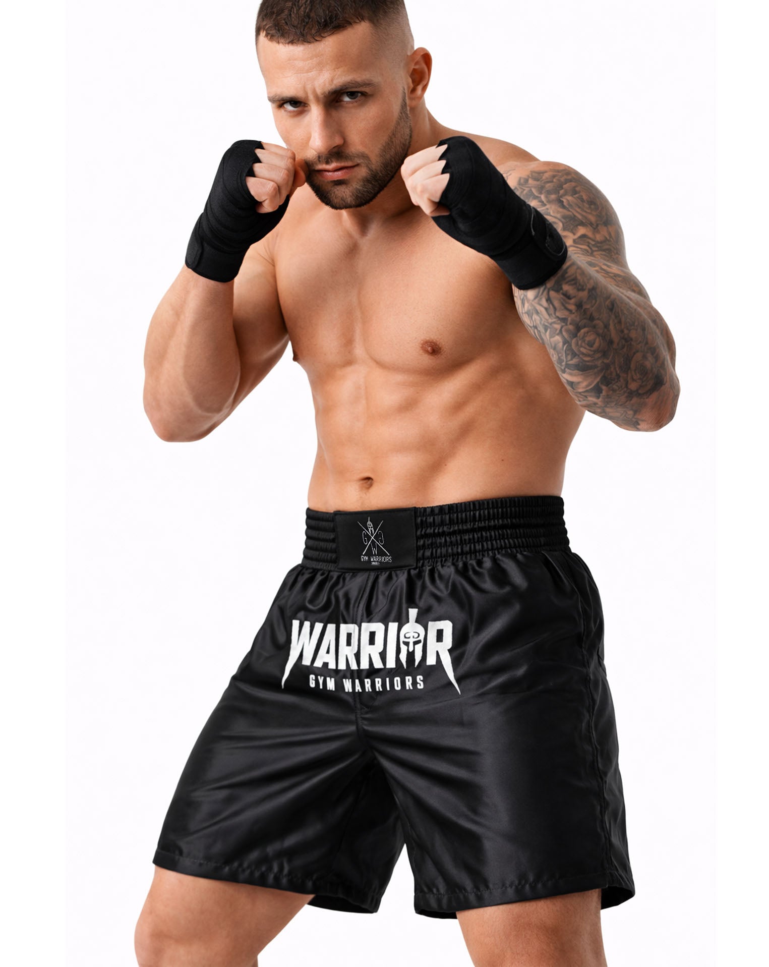 Schwarze Muay Thai Shorts von Gym Generation am Fighter – mit Warrior Print, breitem Bund und Handbandagen in kämpferischer Pose