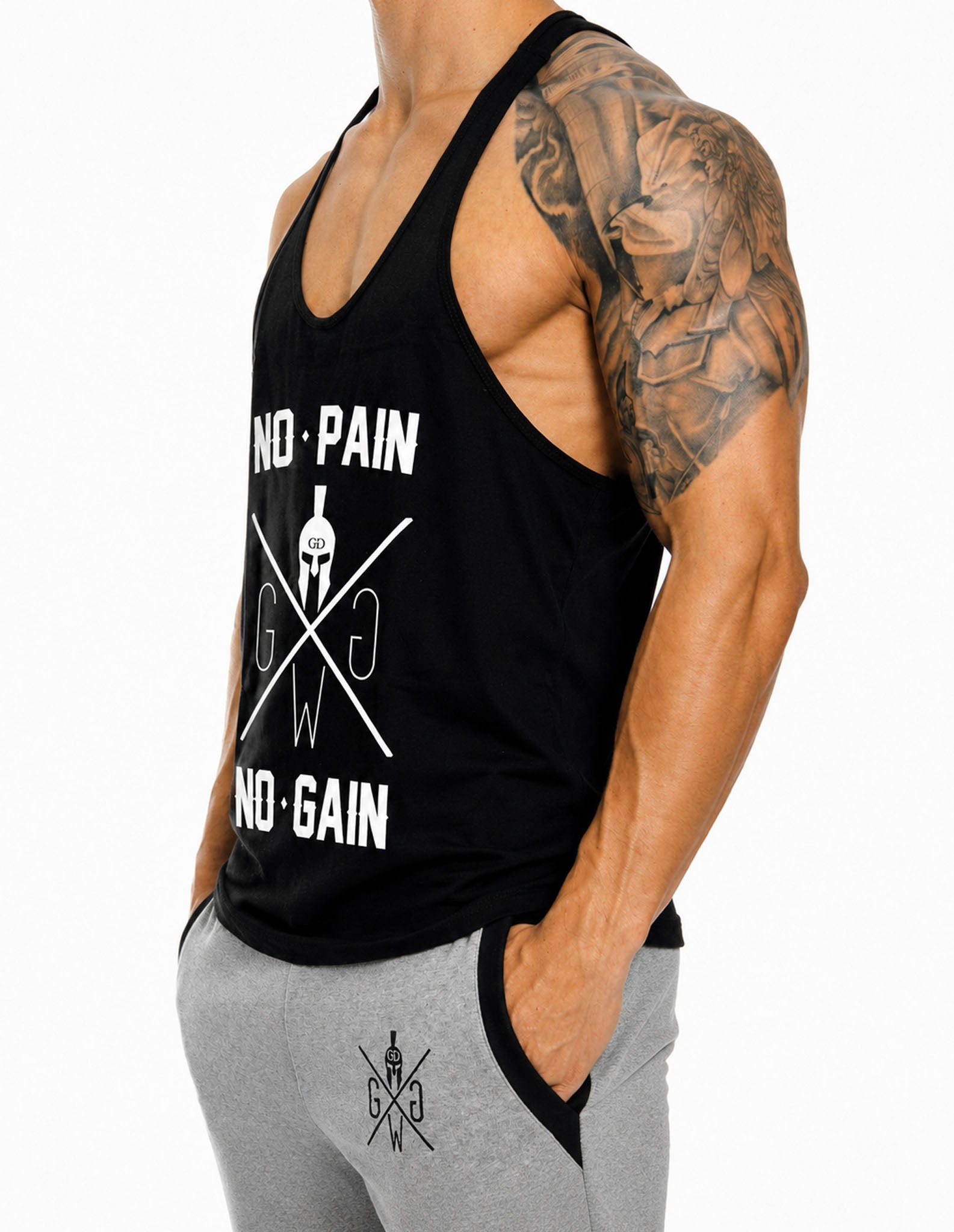 No Pain No Gain Stringer Tank Top von Gym Generation in Schwarz, seitliche Studioansicht mit weissem Frontprint und grauer Trainingshose