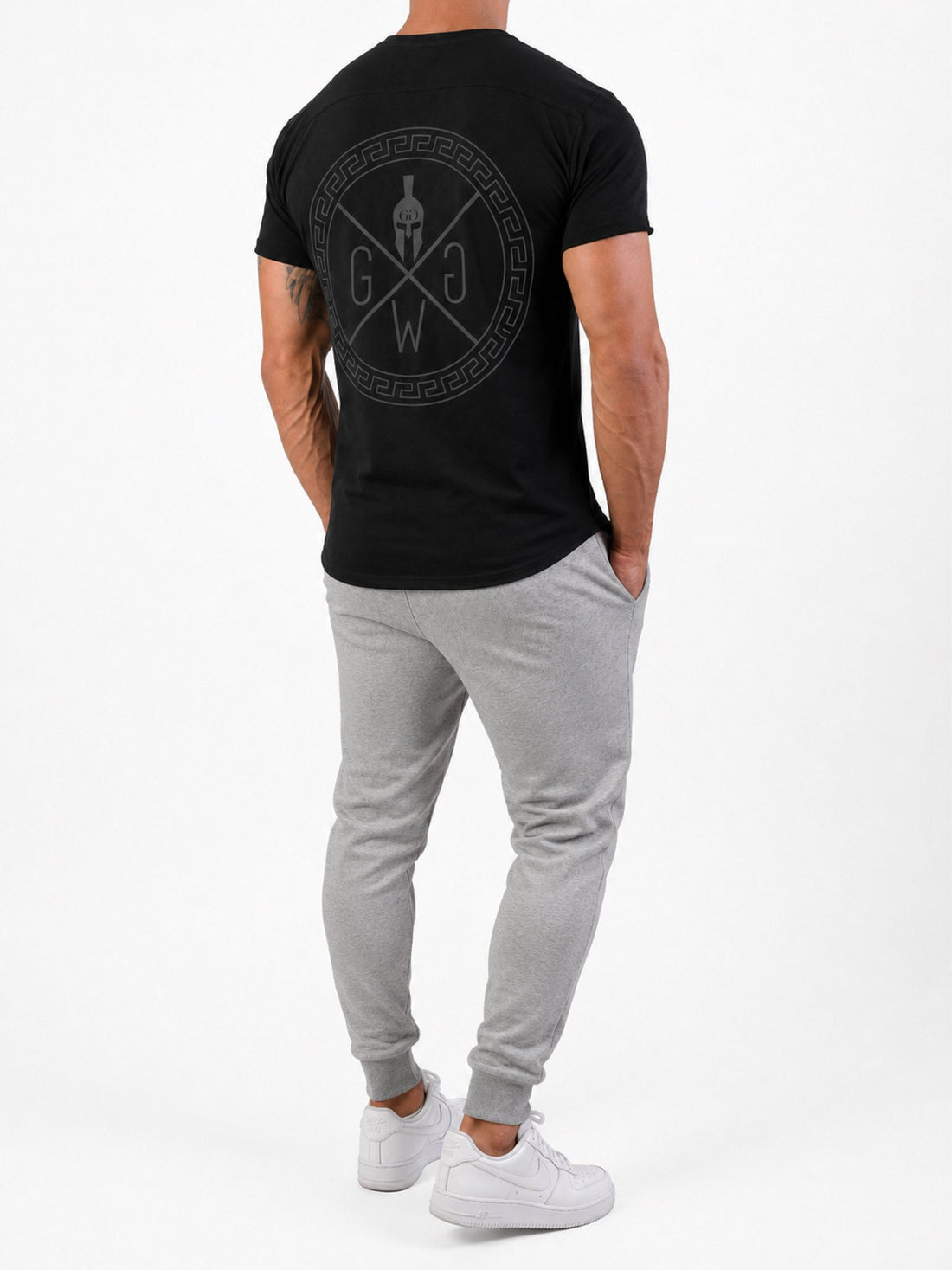 Spartan Gym T-Shirt Herren Schwarz in Ganzkörperansicht von hinten – Mäander-Backprint zu grauem Jogger und Sneakern
