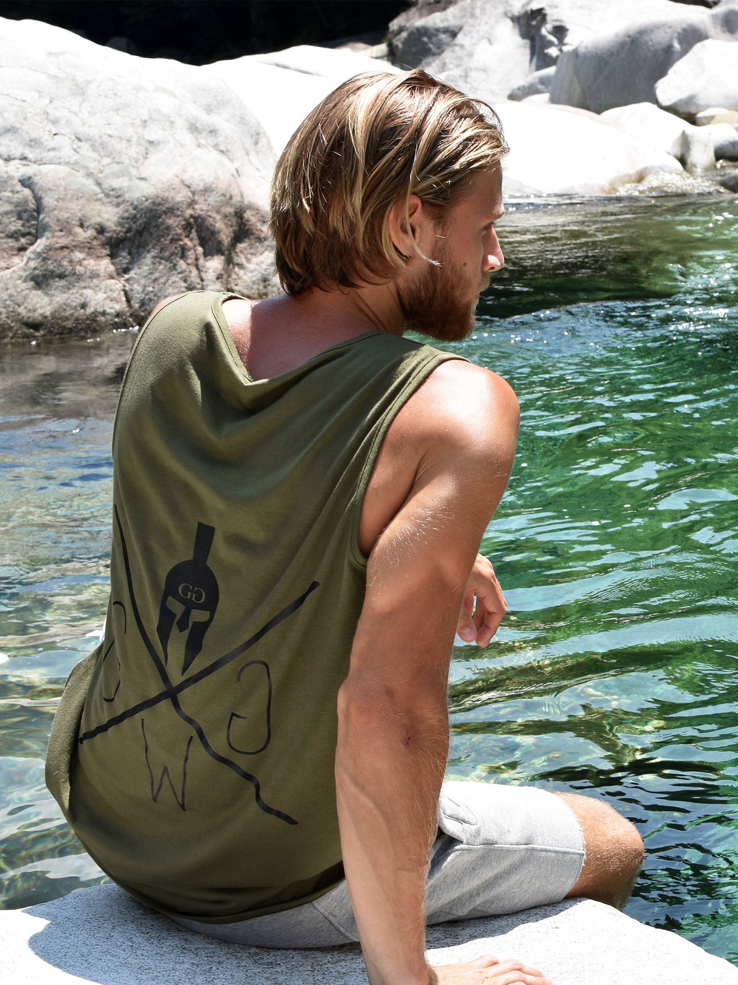 Fitnessmodell am Wasser, trägt das Gym Generation Fitness Tank Top 'Warrior' in Olive mit markantem Gym Warriors Logo auf dem Rücken, ideal für Sommer und Outdoor-Style.