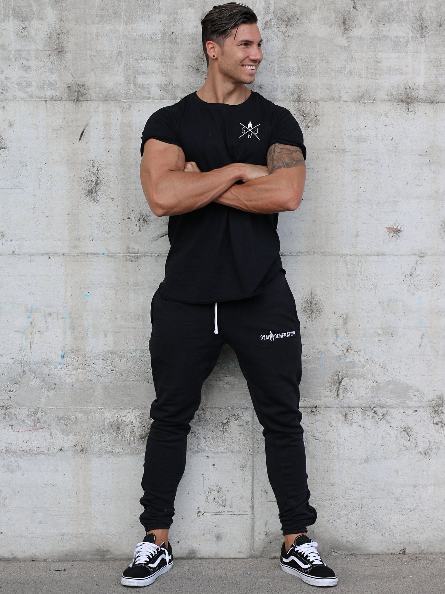 Gym Outfit in Schwarz von Gym Generation – Model präsentiert schwarze Sporthosen und ein schwarzes Sport Shirt, perfekt für den ultimativen Fitnessstudio-Look und intensives Training.