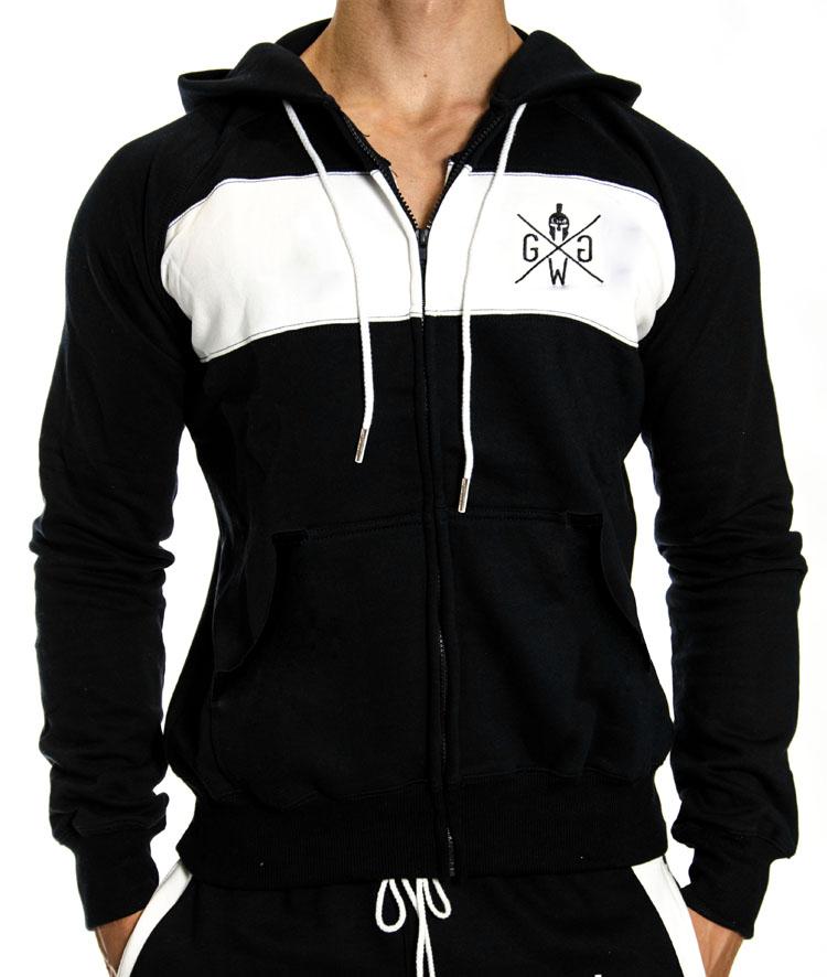 Muskulöser Mann in einer schwarzen und weißen Gym Generation Zip-Jacke mit Logo auf der Brust und Kordelzug, kombiniert mit passenden Jogginghosen, ideal für Sport und Freizeit.